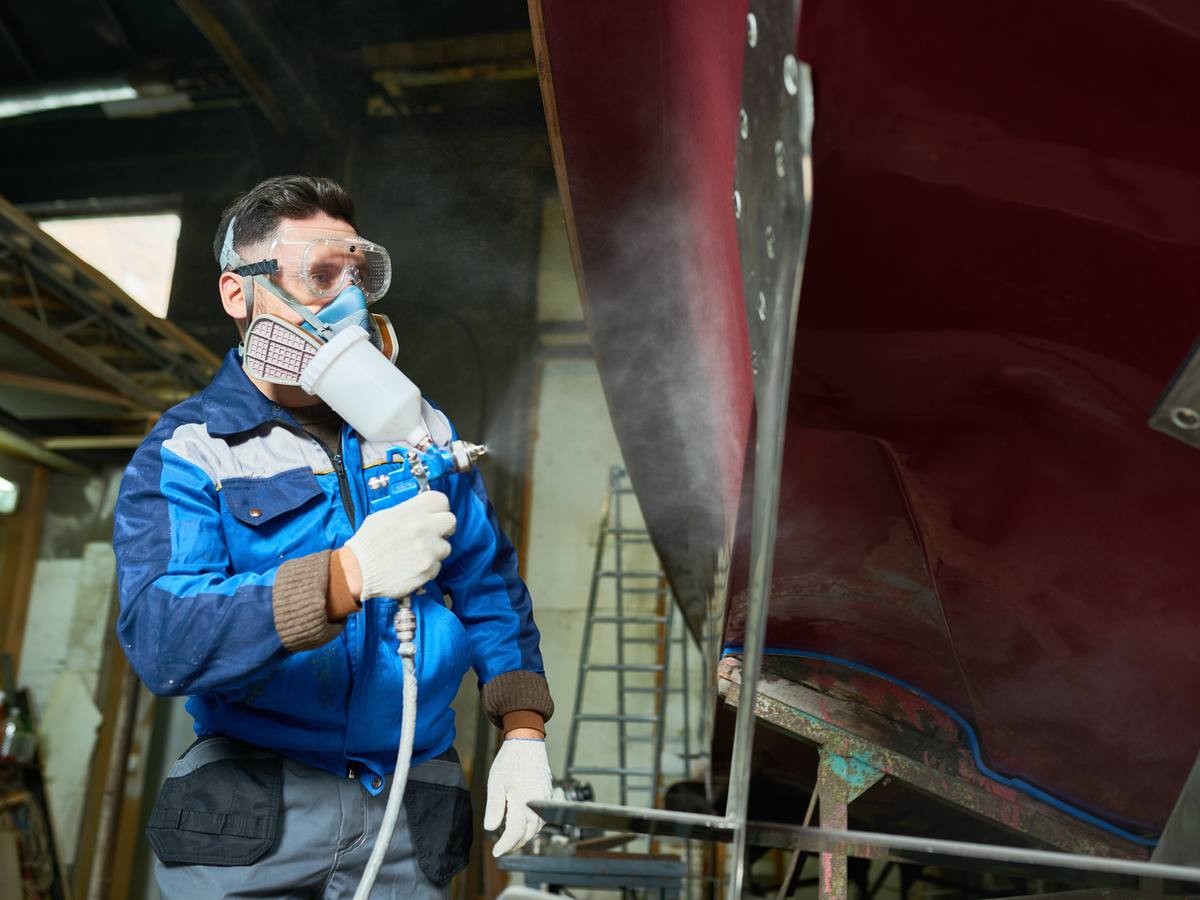 A technician spray-painting a yacht hull during a refit